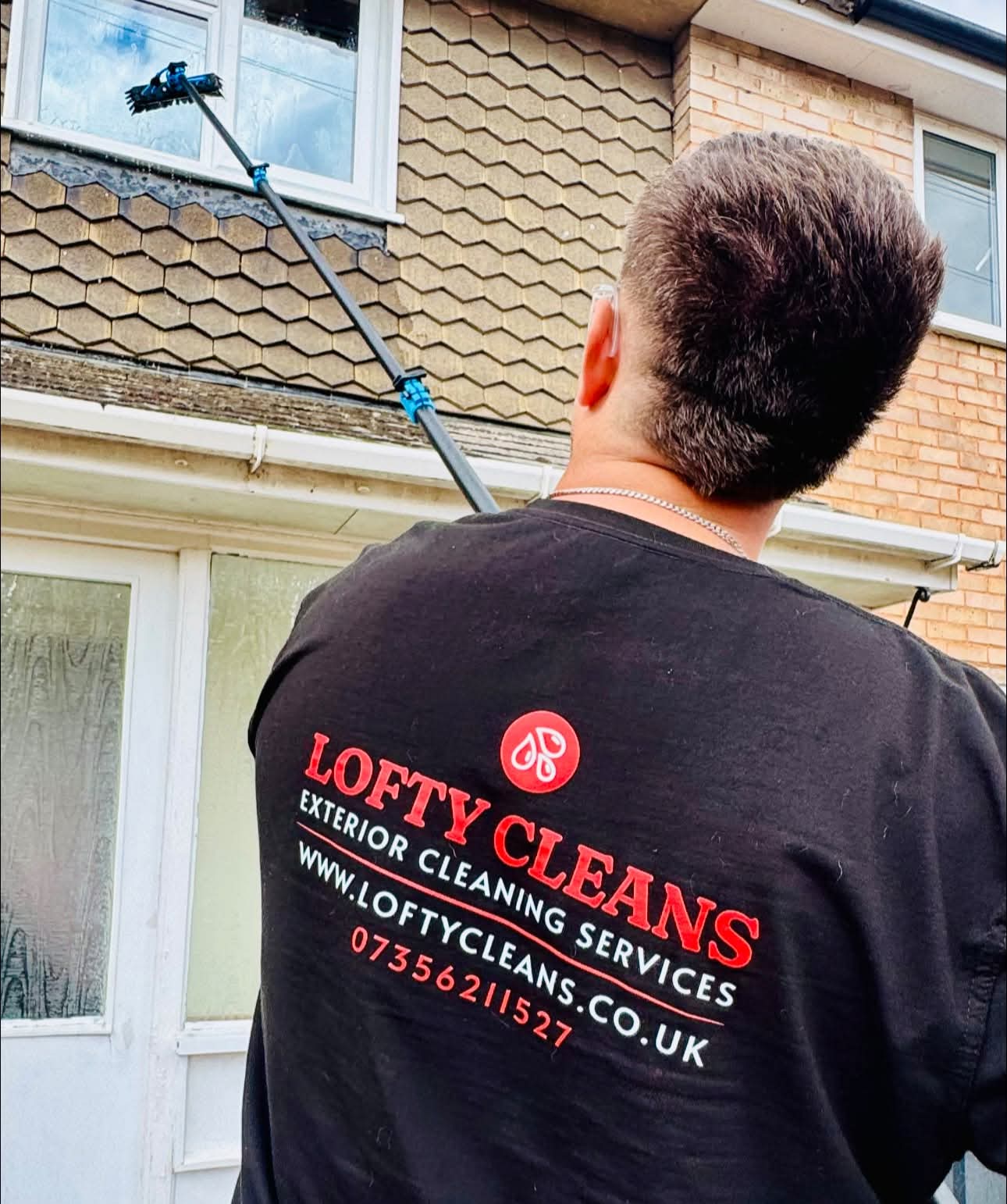 A Lofty Cleans window cleaner using a water fed pole to reach an upper-floor window at a Hereford home